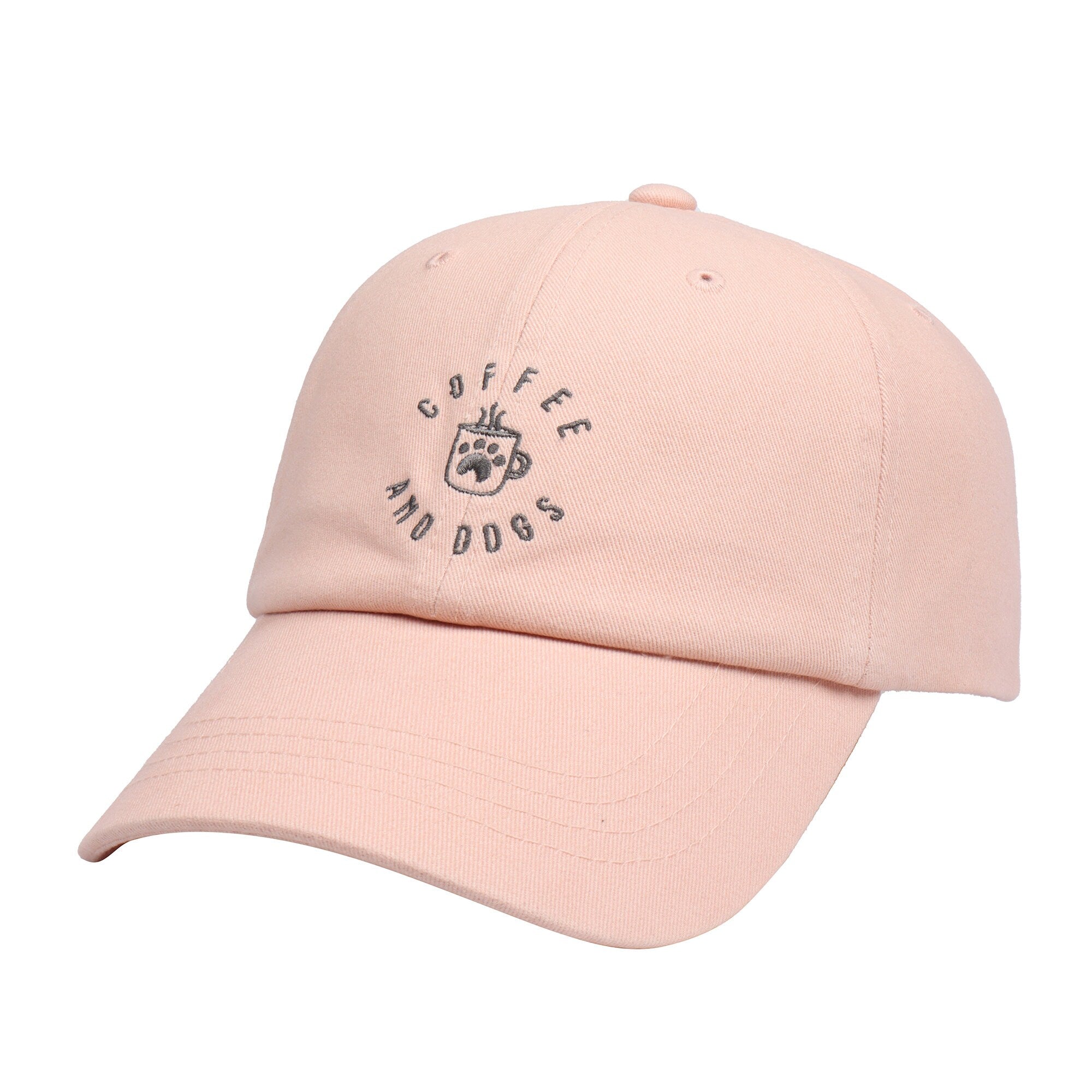 May include: A pink baseball cap with the text 'Coffee and Dogs' embroidered in gray on the front. The text is in a circle with a coffee cup and paw print in the center.