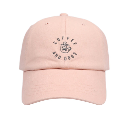May include: A pink baseball cap with the text 'COFFEE AND DOGS' embroidered in gray on the front. The text is in a circle with a coffee cup and paw print in the center.